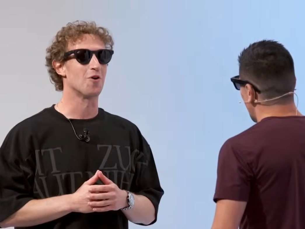 Mark Zuckerberg and mixed martial artist Brandon Moreno, both wearing Ray-Ban Meta glasses, laugh on stage while a screen behind them shows their conversation translated between English and Spanish.
